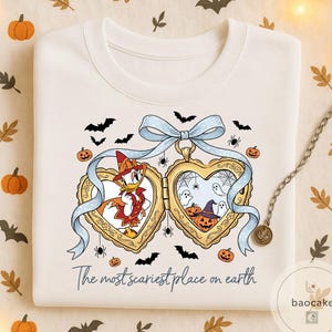 May include: Cream sweatshirt with a Halloween design. The graphic shows a heart-shaped locket with cartoon characters, pumpkins, bats, and spiders. The text "The most scariest place on earth" is printed below the locket.