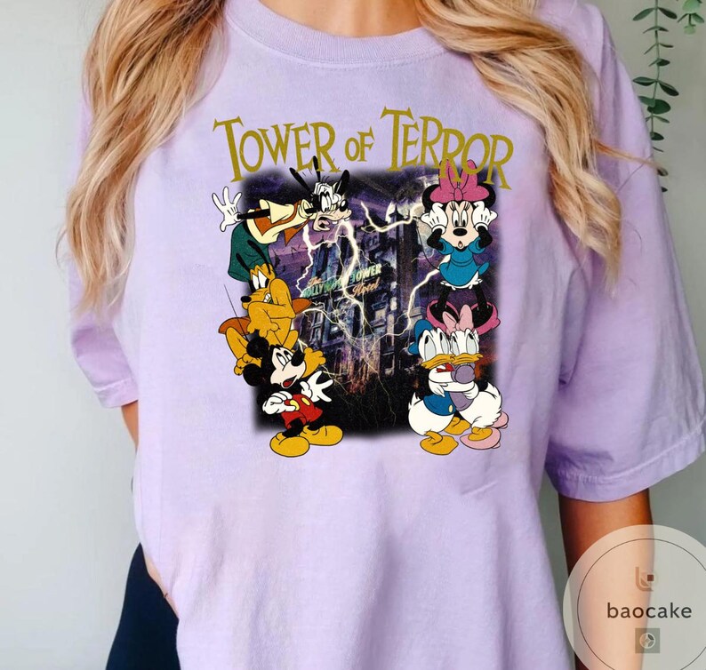 May include: A light purple t-shirt featuring a graphic of Disney characters, including Mickey Mouse, Minnie Mouse, Goofy, and Donald Duck, with the text "Tower of Terror". The graphic has a vintage, cartoon style.