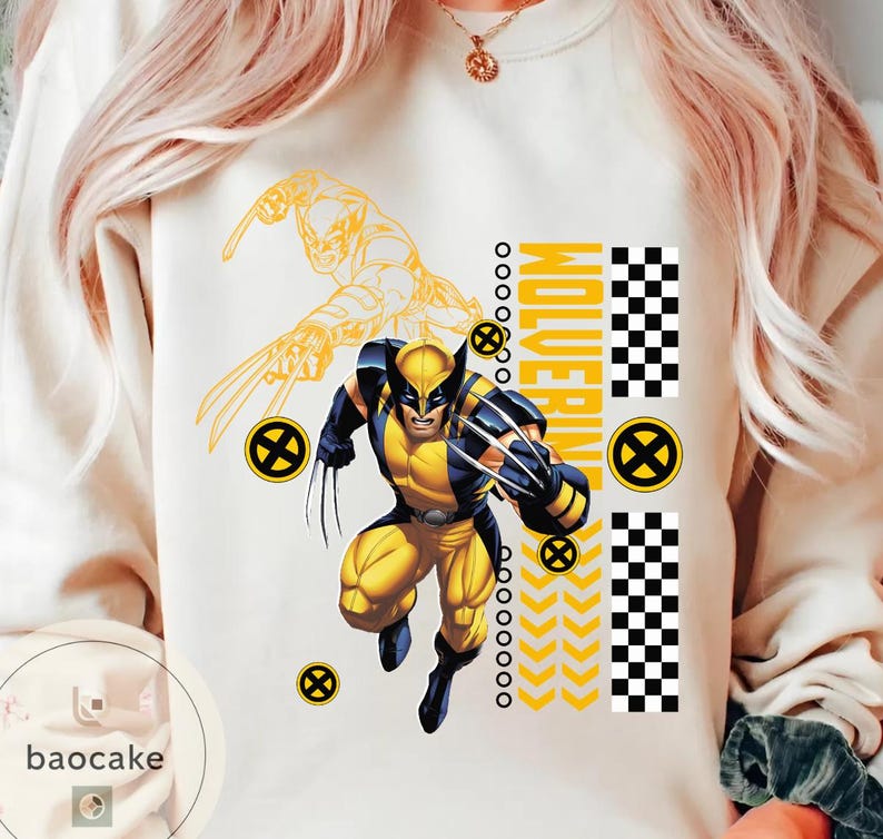 May include: Cream-colored sweatshirt featuring a graphic of Wolverine in a yellow and blue costume with claws extended. The word "Wolverine" is printed vertically in yellow, with additional yellow and black design elements.
