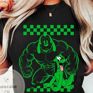May include: Black t-shirt featuring a green cartoon illustration of Pluto in two poses: a muscular version and a sitting version with its tongue out. The design includes a green and black checkered pattern at the top and bottom.