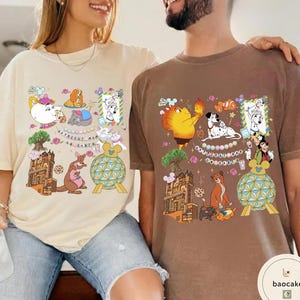 May include: Two t-shirts, one beige and one brown, featuring colorful cartoon designs. The beige shirt has a teapot, kangaroo, and other characters. The brown shirt displays a character holding fire, Dalmatian dogs, and other characters.