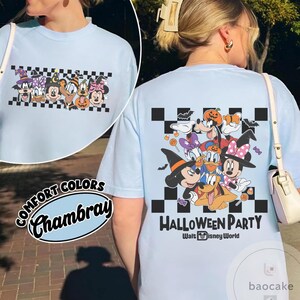 May include: Light blue t-shirt featuring a Halloween-themed graphic with cartoon characters, including Mickey and Minnie Mouse, and the text "HALLOWEEN PARTY Walt Disney World". The shirt has a checkered pattern.