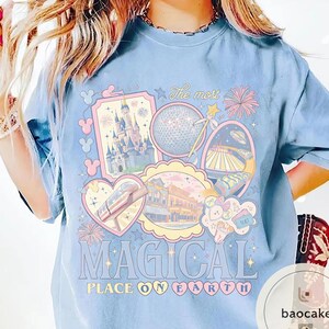 May include: Pale blue t-shirt with a vibrant graphic showcasing theme park imagery, such as a castle and a monorail. The text "The most MAGICAL PLACE ON EARTH" is printed in large letters.