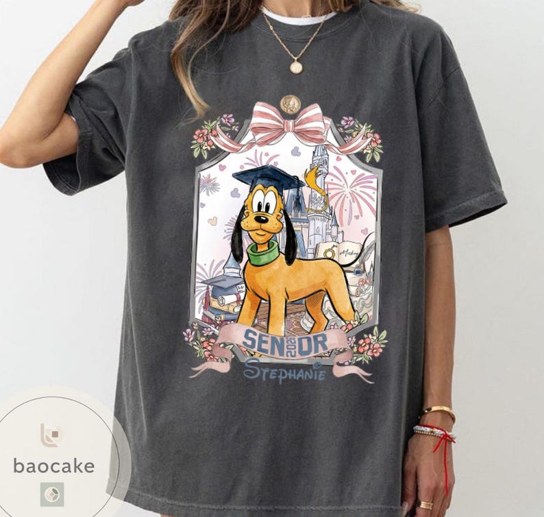 May include: Dark gray t-shirt featuring Pluto the dog wearing a graduation cap, with the text "Senior Stephanie" on a banner. The design includes a castle, fireworks, and floral accents, creating a celebratory theme.