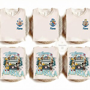 May include: Cream-colored t-shirts with Disney character designs. Some shirts feature an anchor with a character and the word "Name" in blue. Other shirts have a Disney Alaska 2024 design with Mickey and friends.