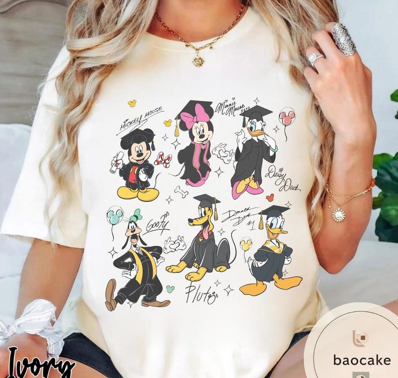 May include: Ivory-colored t-shirt featuring cartoon characters Mickey Mouse, Minnie Mouse, Donald Duck, Daisy Duck, Goofy, and Pluto in graduation attire. The design includes graduation caps, gowns, and celebratory elements.