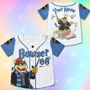 Puede incluir: Camiseta de b&eacute;isbol blanca con mangas azules y rayas finas. Presenta un personaje de dibujos animados de Bowser con una varita, el nombre "Bowser" y el n&uacute;mero "00". La parte trasera tiene un dise&ntilde;o similar con el texto "Your Name".