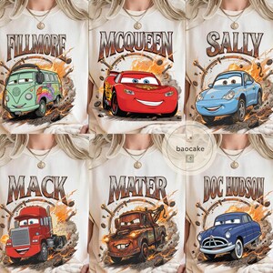 May include: Cream-coloured t-shirts featuring cartoon car characters: Fillmore, McQueen, Sally, Mack, Mater, and Doc Hudson. Each shirt displays a character's name in a vintage-style font, surrounded by a circular design with tools.