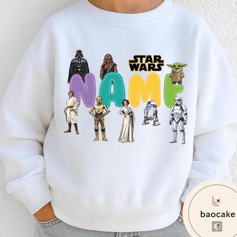 May include: White sweatshirt featuring Star Wars characters and the word "NAME" in colorful letters. Characters include Darth Vader, Chewbacca, Yoda, and others. The Star Wars logo is also visible.