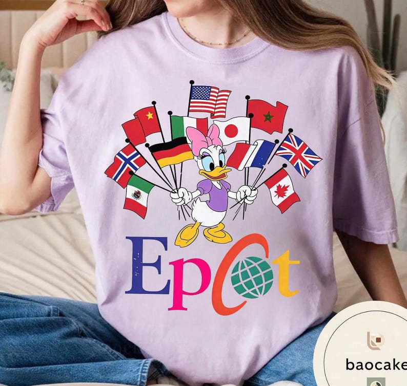 May include: A lilac t-shirt with a Daisy Duck graphic holding flags of different nations. The word "Epcot" is printed in colourful letters below the character, with a globe graphic. The shirt has a relaxed fit.