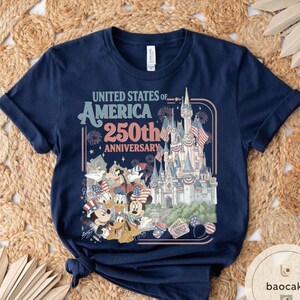 May include: Navy blue t-shirt with a graphic celebrating the 250th anniversary of the United States of America. The design includes a castle, fireworks, and cartoon characters like Mickey and Minnie Mouse.