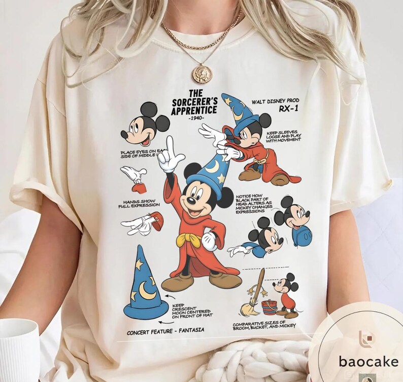 May include: Cream-colored t-shirt featuring a graphic of Mickey Mouse in his Sorcerer's Apprentice attire. The design includes illustrations and text detailing Mickey's features and the film's elements. The text includes "The Sorcerer's Apprentice - 1940".