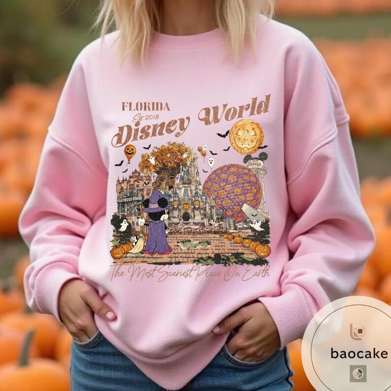 Op de afbeelding: Roze sweatshirt met een afbeelding van Disney World in Florida, met Mickey Mouse in een heksenpak, pompoenen en de tekst "The Most Scariest Place On Earth". Het sweatshirt heeft lange mouwen.