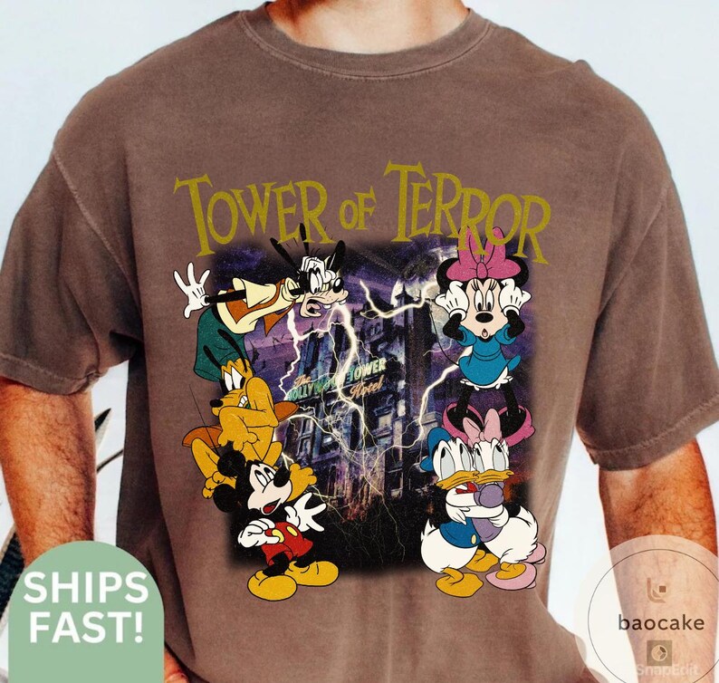 May include: Brown t-shirt featuring a graphic of Disney characters, including Mickey Mouse, Minnie Mouse, Goofy, Donald Duck, and Pluto, with the text "Tower of Terror". The design includes a purple lightning effect and a building.