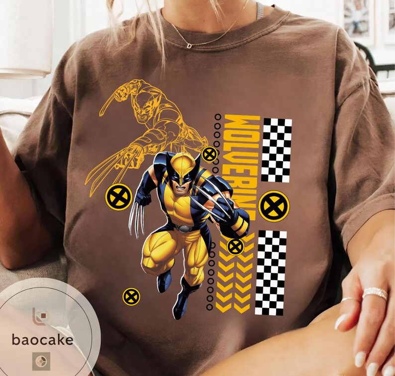 May include: Brown t-shirt featuring a Wolverine graphic in yellow and blue. The design includes a detailed illustration of Wolverine in action, the word "Wolverine", and a checkered pattern. The shirt has a crew neck and short sleeves.
