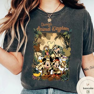 May include: Dark gray t-shirt featuring a graphic of Disney's Animal Kingdom characters, including Mickey and Minnie Mouse, Donald Duck, Goofy, and Pluto. The design is set against a jungle backdrop with the park's logo.