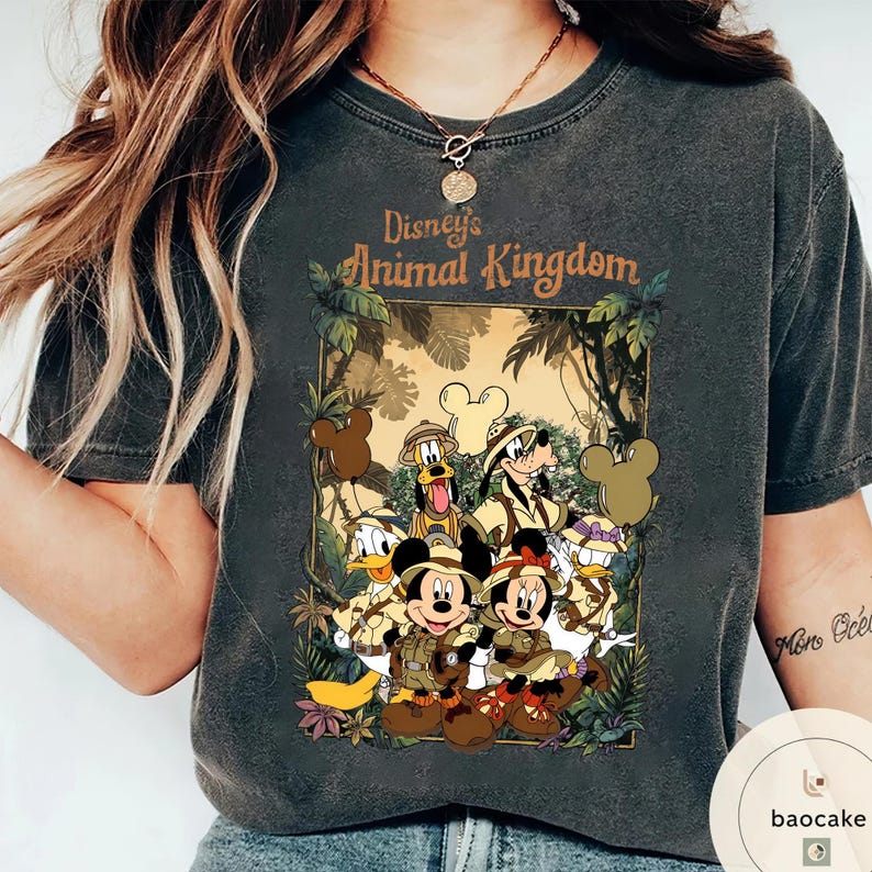 May include: Dark gray t-shirt featuring a graphic of Disney's Animal Kingdom characters, including Mickey and Minnie Mouse, Donald Duck, Goofy, and Pluto. The design is set against a jungle backdrop with the park's logo.