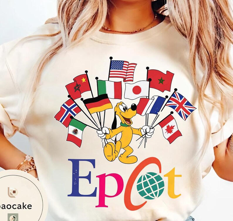 May include: Cream-coloured t-shirt with a cartoon Pluto holding flags from various countries, including the United States, Japan, Italy, and the United Kingdom. The word "Epcot" is printed in colourful letters below the cartoon.
