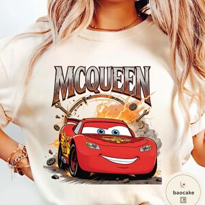 May include: Cream-coloured t-shirt featuring a graphic of Lightning McQueen from the film Cars. The design includes the word "MCQUEEN" in a distressed font, along with racing details and a smiling red car.