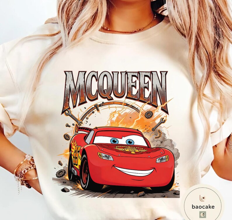 May include: Cream-coloured t-shirt featuring a graphic of Lightning McQueen from the film Cars. The design includes the word "MCQUEEN" in a distressed font, along with racing details and a smiling red car.