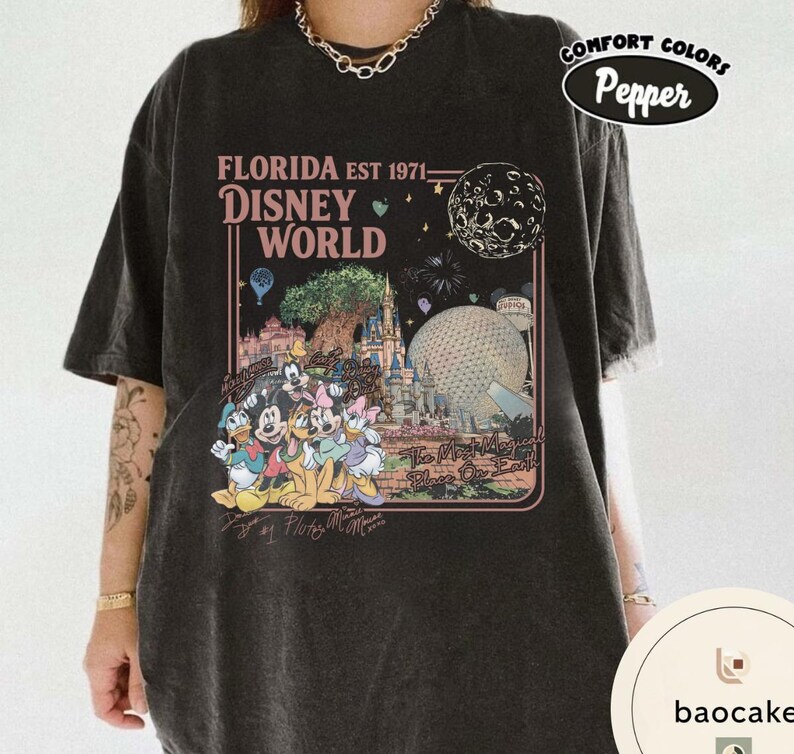 May include: A charcoal black short-sleeve t-shirt featuring a graphic print with the text FLORIDA EST 1971 DISNEY WORLD and The Most Magical Place On Earth. The design includes illustrations of Disney characters, the castle, and Epcot.