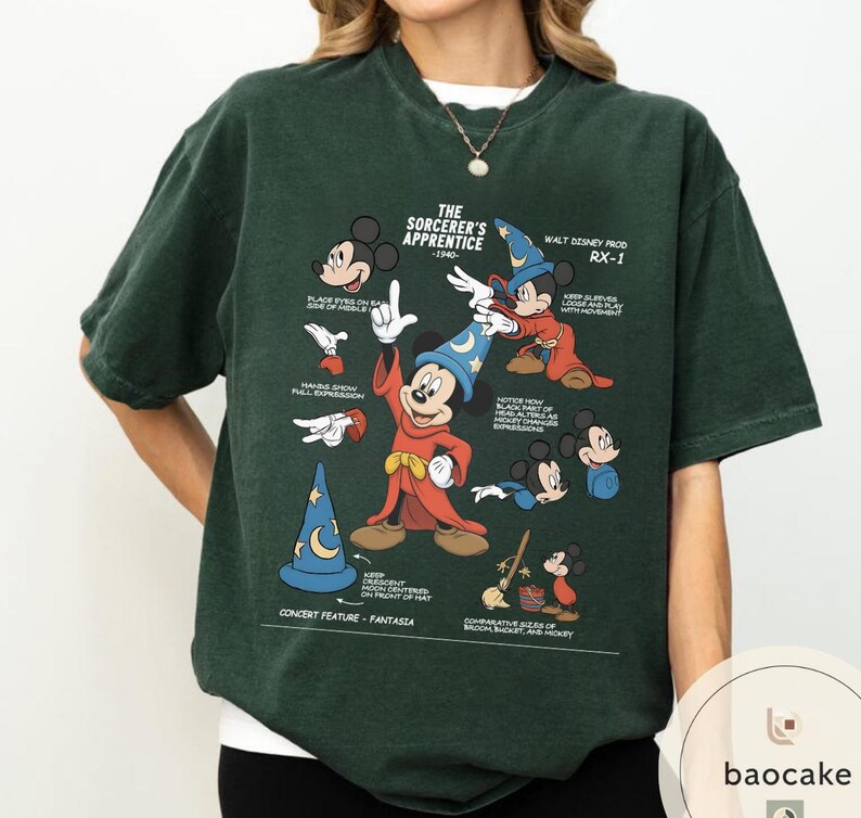May include: Dark green t-shirt featuring a graphic of Mickey Mouse from "The Sorcerer's Apprentice." The design includes illustrations of Mickey in various poses, a wizard hat, and text. The shirt has short sleeves and a crew neck.
