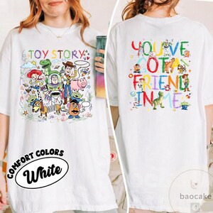 May include: White t-shirt featuring colorful illustrations of Toy Story characters on the front and back. The front design includes the text "TOY STORY" and the back says "YOU'VE GOT A FRIEND IN ME". The shirt also has the text "COMFORT COLORS White".