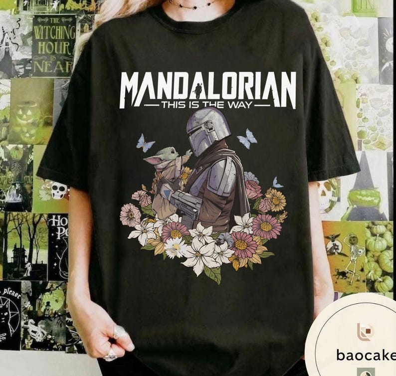Puede incluir: Camiseta negra con un dise&ntilde;o de The Mandalorian y Grogu, rodeados de flores y mariposas. El texto "MANDALORIAN - THIS IS THE WAY" est&aacute; impreso en la parte superior. La camiseta es de color oscuro.
