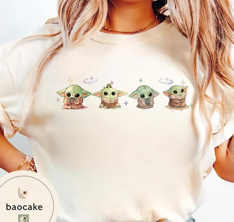 May include: Cream-colored sweatshirt featuring four cartoon Grogu characters in various poses. Each Grogu is green with large eyes and is surrounded by small stars and a ring. The baocake logo is visible in the lower left corner.