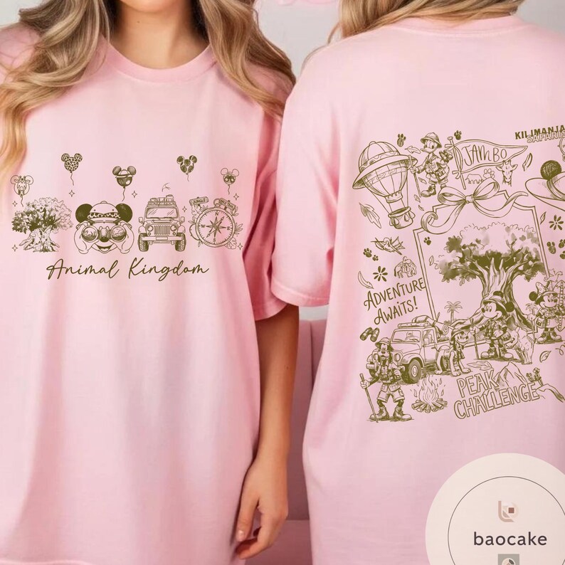 May include: Pink t-shirts with a green graphic design. The front of the shirt says "Animal Kingdom" with illustrations of Mickey Mouse, a jeep, and a compass. The back of the shirt says "Adventure Awaits!" with illustrations of a hot air balloon, Mickey Mouse, and a jeep.