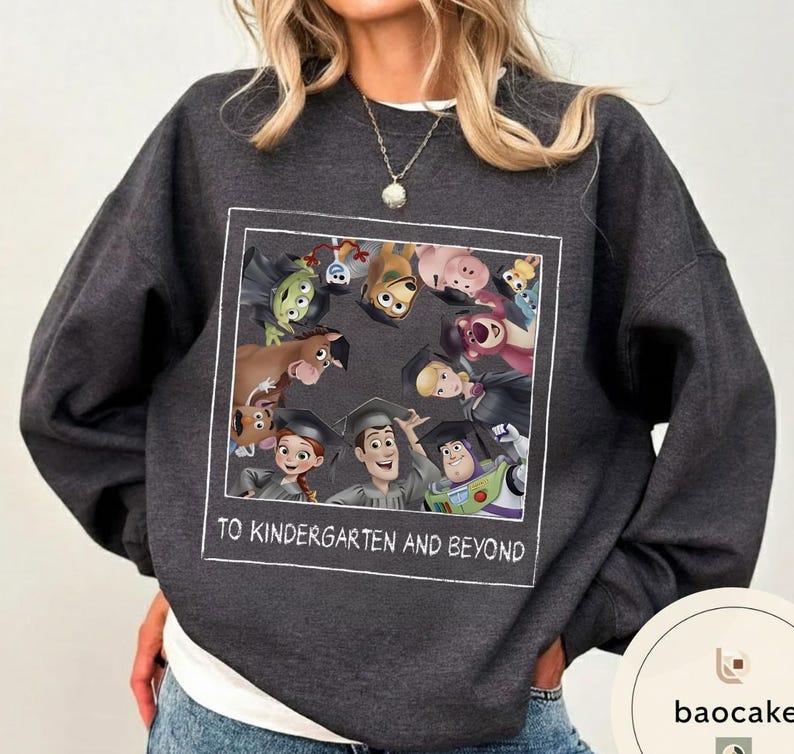 May include: Dark grey sweatshirt with a graphic of animated characters wearing graduation caps. The image includes characters from a popular animated movie. The text "TO KINDERGARTEN AND BEYOND" is printed in white.