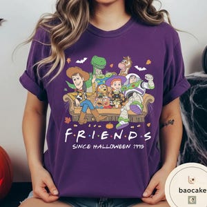 May include: A purple t-shirt featuring a graphic of Toy Story characters sitting on a couch with the text "F.R.I.E.N.D.S SINCE HALLOWEEN 1995". The design includes Woody, Buzz Lightyear, Jessie, Rex, Slinky Dog, Mr. Potato Head, and Bullseye.