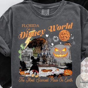 May include: Dark gray t-shirt featuring a Halloween-themed design with the text "Florida Disney World" and "The Most Scariest Place On Earth." The graphic includes a castle, Mickey Mouse, pumpkins, and a jack-o'-lantern.