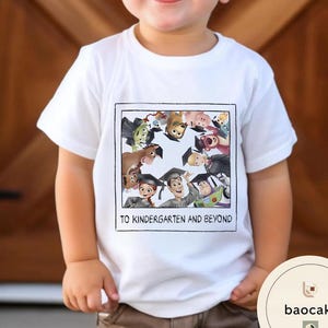 May include: White t-shirt with a colourful graphic of animated characters wearing graduation caps. The text "TO KINDERGARTEN AND BEYOND" is printed below the graphic. The shirt is worn by a child.