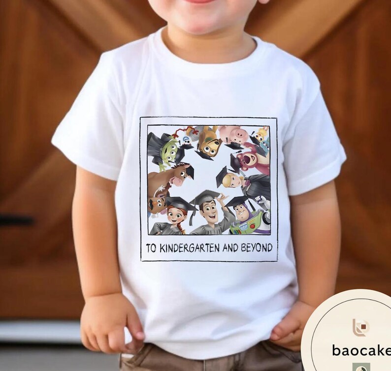 May include: White t-shirt with a colourful graphic of animated characters wearing graduation caps. The text "TO KINDERGARTEN AND BEYOND" is printed below the graphic. The shirt is worn by a child.