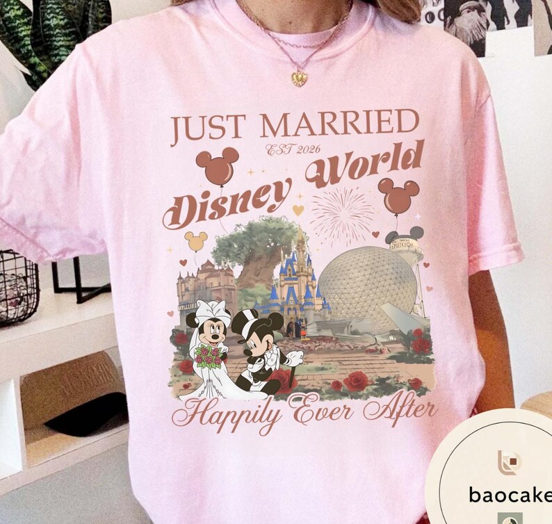 May include: A light pink t-shirt with a graphic featuring Mickey and Minnie Mouse in wedding attire, the words "Just Married Disney World" and "Happily Ever After". The design includes iconic Disney World landmarks and Mickey Mouse balloons.