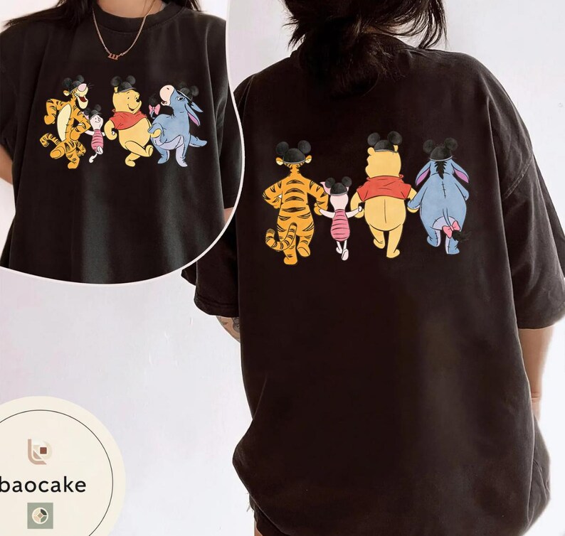 May include: Black t-shirt featuring a cartoon graphic of Winnie the Pooh, Tigger, Piglet, and Eeyore. The front shows the characters in a line, and the back shows the same characters. The characters are wearing Mickey Mouse ears.