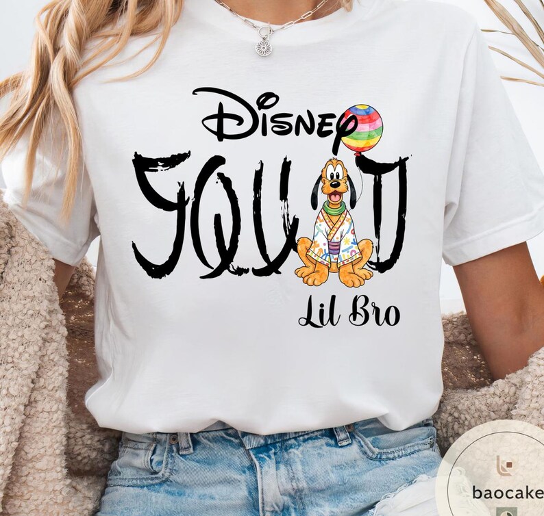 Puede incluir: Camiseta blanca con un dise&ntilde;o negro que dice "Disney Squad" con una imagen de dibujos animados de Pluto sosteniendo un globo arco&iacute;ris. Las palabras "Lil Bro" est&aacute;n impresas debajo.