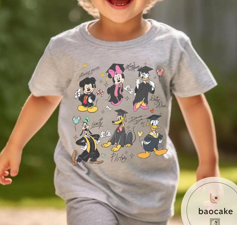 May include: A light gray t-shirt featuring a colorful graphic of Disney characters in graduation attire. Mickey Mouse, Minnie Mouse, Donald Duck, Goofy, and Pluto are depicted with graduation caps and gowns. The shirt has the text "Mickey Mouse" and character names.