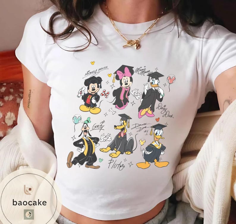 May include: White t-shirt featuring cartoon characters Mickey Mouse, Minnie Mouse, Donald Duck, Daisy Duck, Goofy, and Pluto in graduation attire. The characters are wearing graduation caps and gowns, with some holding balloons. The shirt has the text "Mickey Mouse", "Minnie Mouse", "Daisy Duck", and "Pluto".