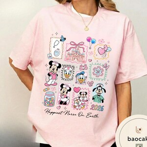 May include: Pink t-shirt featuring cartoon characters and medical-themed illustrations. The shirt includes images of Mickey and Minnie Mouse, Donald Duck, and Goofy in nurse attire, along with a castle, balloons, and the text "Happiest Nurse On Earth" and the year "2026".