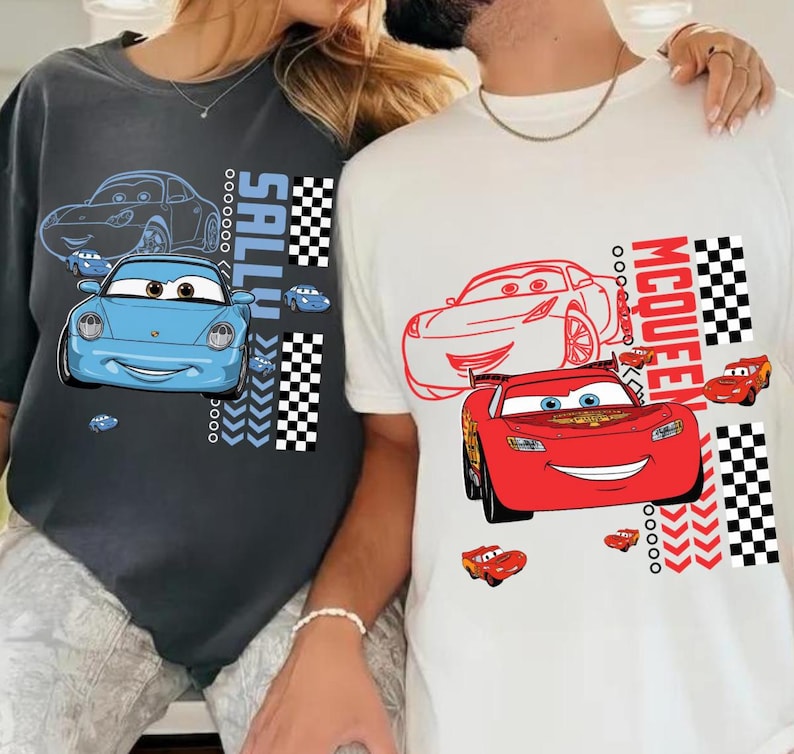 May include: Two t-shirts with cartoon car designs. One is dark grey with a blue car and the name "SALLY". The other is white with a red car and the name "MCQUEEN". Both shirts feature a chequered flag design.