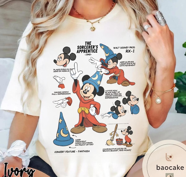 May include: Ivory-colored t-shirt featuring a graphic of Mickey Mouse as the Sorcerer's Apprentice from Fantasia. The design includes illustrations and text detailing the character's features and the film's production details.
