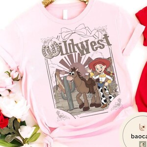 Pu&ograve; includere: T-shirt rosa chiaro con grafica Wild West. La grafica include un'immagine a cartoni animati di una cowgirl con un lazo, un cavallo e la scritta "Wild West". Il design &egrave; incorniciato da un ferro di cavallo e un fiocco.