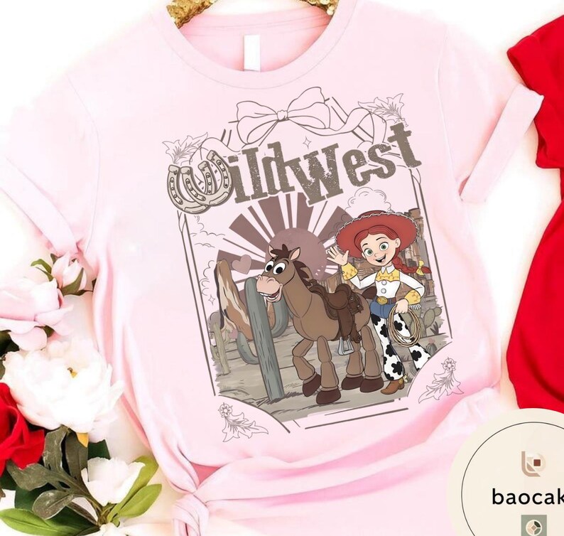 Pu&ograve; includere: T-shirt rosa chiaro con grafica Wild West. La grafica include un'immagine a cartoni animati di una cowgirl con un lazo, un cavallo e la scritta "Wild West". Il design &egrave; incorniciato da un ferro di cavallo e un fiocco.
