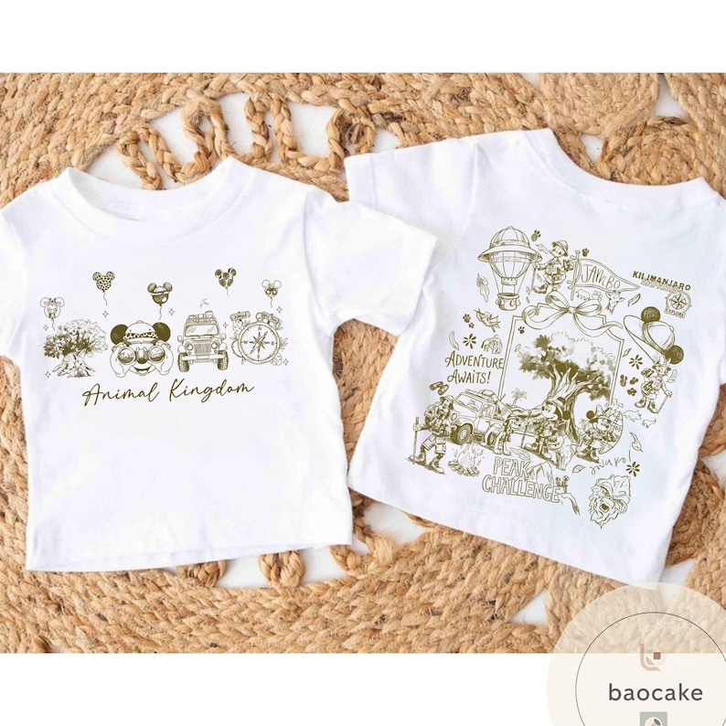 May include: Two white t-shirts with gold-colored graphics. One shirt says "Animal Kingdom" with Mickey Mouse and other park icons. The other shirt says "Adventure Awaits!" with a safari theme and "Kilimanjaro" text.