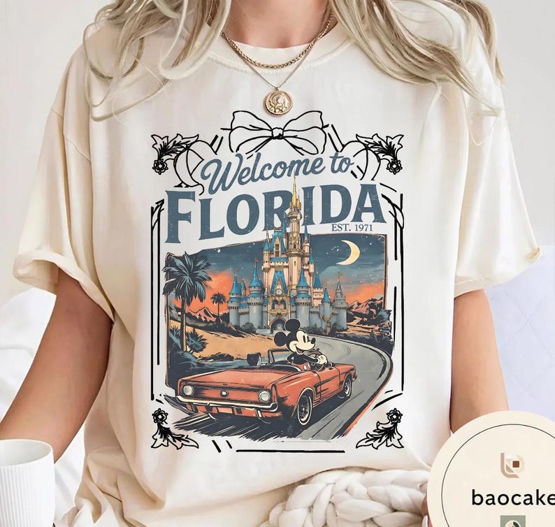 May include: Cream-colored t-shirt featuring a graphic of Mickey Mouse driving a red convertible towards a castle. The text "Welcome to Florida" and "EST. 1971" are displayed above the image in a decorative frame.