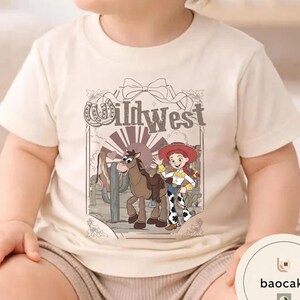 Pu&ograve; includere: T-shirt beige con un'illustrazione a cartoni animati di un cavallo, una cowgirl e la scritta "Wild West". Il disegno &egrave; ambientato su uno sfondo desertico. La maglietta &egrave; realizzata in tessuto morbido e chiaro.