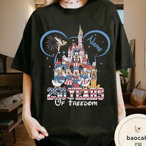 Peut inclure: T-shirt noir avec un motif patriotique Disney. Le motif comprend un ch&acirc;teau, des feux d'artifice et le texte "250 YEARS Of Freedom". Mickey Mouse, Donald Duck et d'autres personnages sont v&ecirc;tus de rouge, de blanc et de bleu.