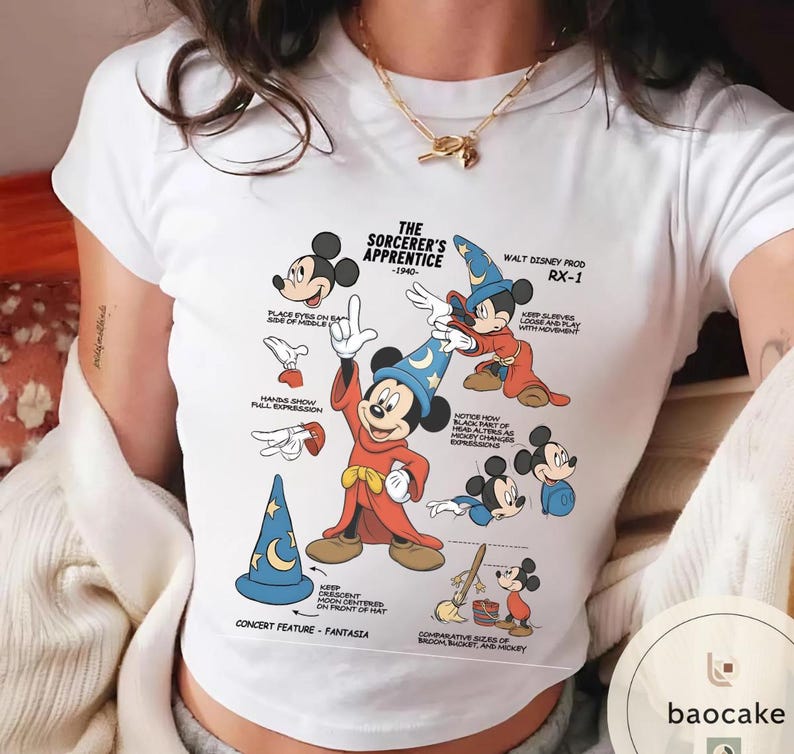 May include: White t-shirt featuring a graphic of Mickey Mouse from "The Sorcerer's Apprentice" (1940). The design includes various poses of Mickey in his sorcerer attire, with text annotations. The shirt has a crew neck.